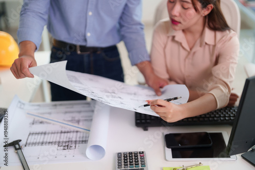 Asian architects engineers adult male female review blueprints design construction project plans collaborate office meeting teamwork discuss ideas solution focus work