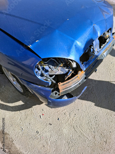 Abandoned wreck of a car sitting on a street in a city during midday with visible damage and rust