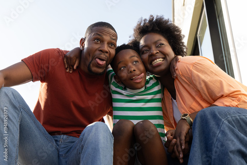 African American family with child crouching on steps leaning in making playful faces wearing watch