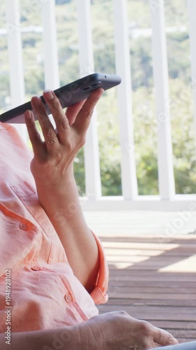 Vertical video: Answering call, woman in peach with phone at mouth, moving out on porch, copy space