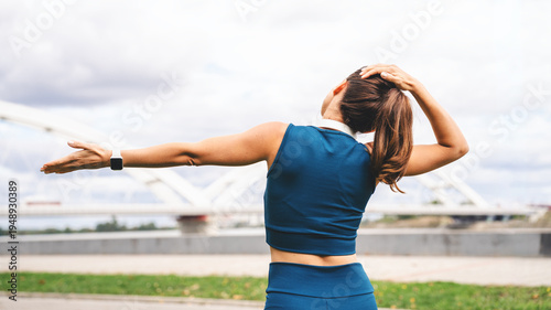 Rear view of a fit woman performing a warm-up stretch outdoors in urban environment.