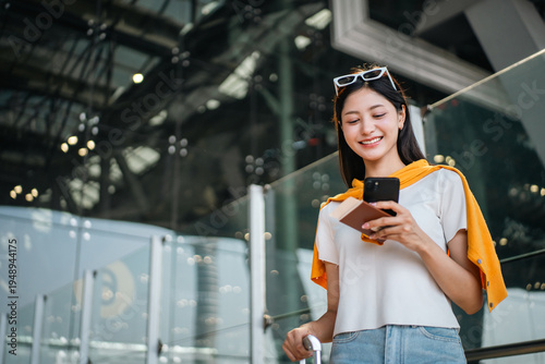 Foto Young asian woman traveler using smartphone for checking flight information check the routes trip while waiting with her luggage at the airport terminal
