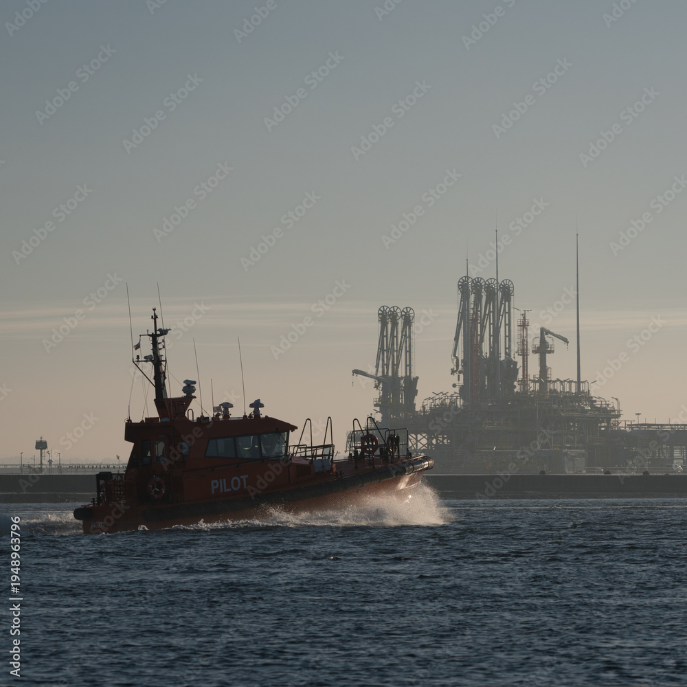 Fototapeta premium MARITIME TRANSPORT - A pilot boat sails against the backdrop of a gas terminal