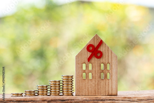 Increasing stacks of coins and house model with percent sign, representing home loan, property tax, and financial growth.