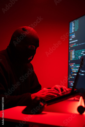Hacker in balaclava with an obscured face is stealing data, representing cybercrime, hacking, dark web activity, and online security threats. Cyber Security concept.