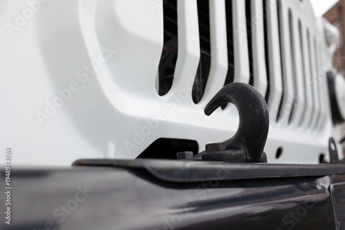  Close-up of a heavy-duty black metal tow hook on the front bumper of a white off-road vehicle.  Steel towing hook on a 4x4 car, selective focus and blurred background.
