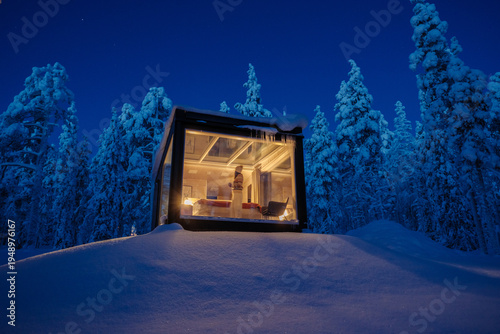 Cozy glass cabin surrounded by snowy forests in Akaslompolo, Lapland during a winter evening
