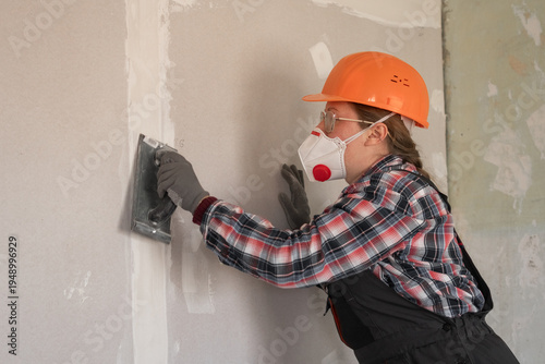 Woman builder repairman with an emery tool sanding a plastered wall