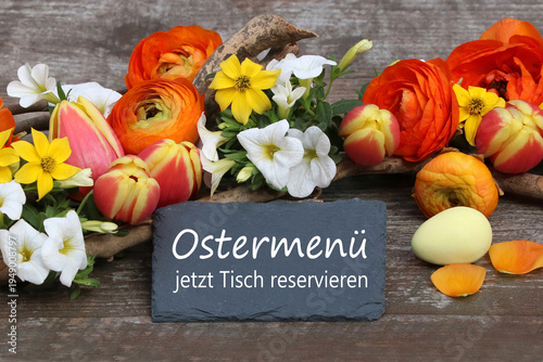 Tafel mit der Aufschrift Ostermenü jetzt Tisch reservieren umgeben von Blumen.
