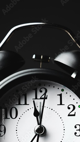 Timelapse of black and white vintage alarm clock on black background. Old fashioned alarm clock with bells. Time moving fast. Vertical video. Time concept. Close-up in 4K, UHD