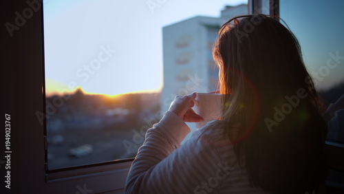 brunette woman drinking coffee on the balcony at sunset, back view. view from the window to the sunset, have fun and enjoy