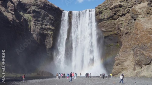 Majestic Skógafoss waterfall with a rainbow and tourists at the base.