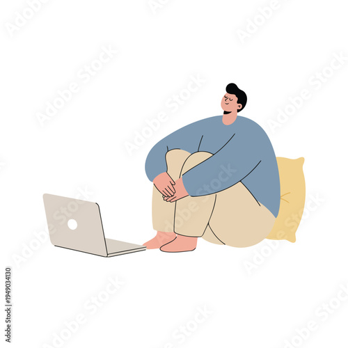 A person sits comfortably on the floor with knees hugged, leaning against a yellow pillow, engrossed in content on a laptop.