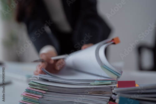 Businesswoman's hands with a pen flipping pages through a tall stack of file folders with colorful tabs on a minimalist desk, conveying organization, workload and deadlines