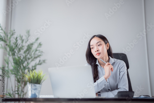 Obraz na plátně Young Asian woman sits at her desk, contemplating a problem or idea while workin