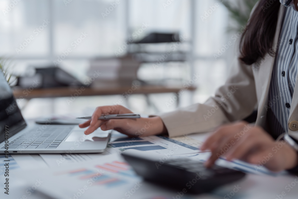 Fototapeta premium Businesswoman's hands are busy calculating financial data, analyzing reports, and typing on a laptop, emphasizing efficiency and accuracy in bookkeeping, accounting, and corporate strategy