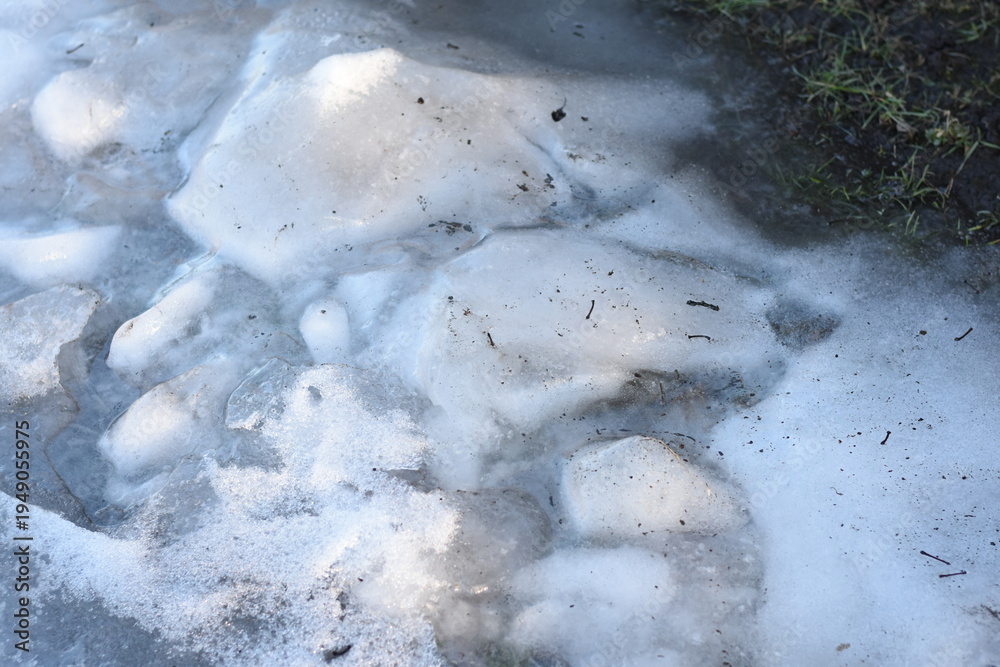Obraz premium Horizontal photo of spring ice remnants partially bordering grass. Transition from ice to greenery.