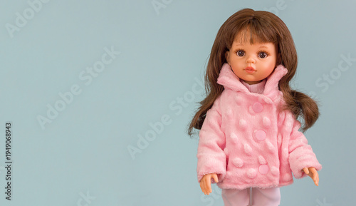A realistic vinyl toy doll with beautiful dark hair and stylish clothes on a blue background, copy space for text