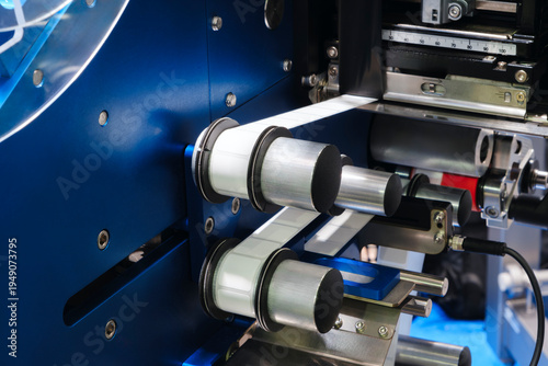 Blue industrial machine with precise rollers. Metal parts move in synchronized motion. Mechanical precision dominates the scene. Ideal for manufacturing or automation contexts