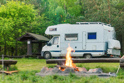 Camping on nature with cozy campfire and motorhome in serene forest setting
