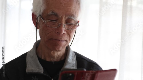 Slow motion of senior Japanese man with glasses using smartphone at home, cinematic lifestyle, silver generation, farsightedness, focused expression, elderly, 4K 30p, natural light.