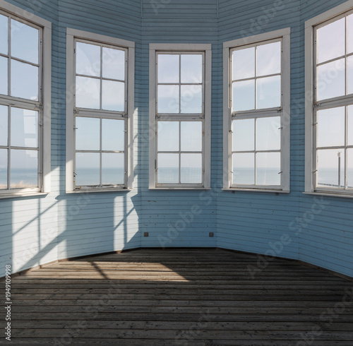 Empty interior of a light blue wooden gazebo featuring large windows with a view of the distant sea horizon