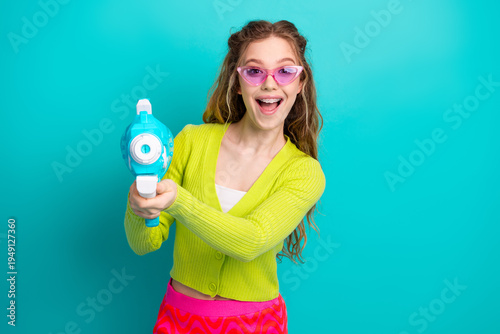 Fotografie Excited young woman holding a toy water gun on a turquoise background, showcasin