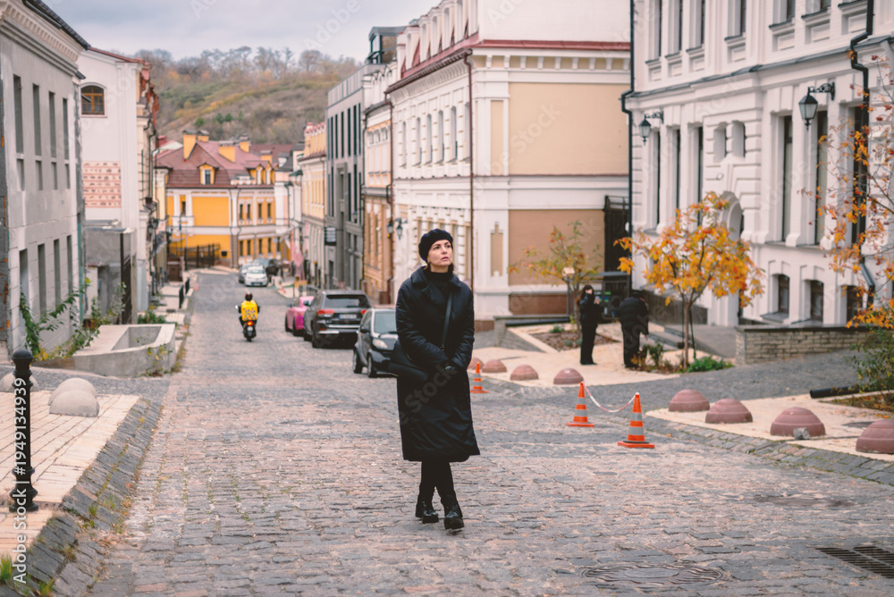 Obraz premium Elegant Woman in Black Coat and Beret Walking Down Old Cobblestone Street in Kyiv, Ukraine - Autumn Urban Lifestyle
