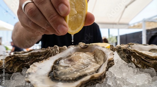 Fotografi POV close up of a hand squeezing a fresh yellow lemon half over a raw oyster on the half shell