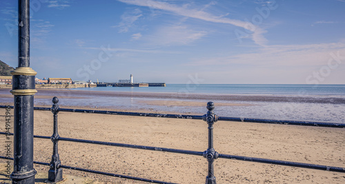 A scene of a beach with a lighthouse and railings in the foreground.