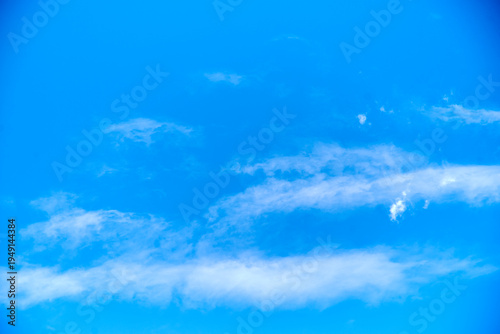 Bright blue sky background with diffuse white clouds and copy space.