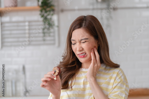 Young Asian woman feels a sudden toothache while eating a cookie. She shows pain from a toothache after eating sweets, highlighting dental sensitivity problems.