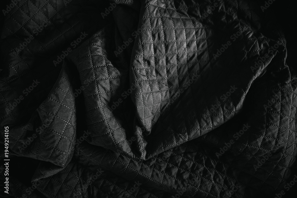 Obraz premium Close-up of black quilted bedsheet fabric in dramatic low light. Textured textile surface with deep shadows highlighting stitching pattern and soft folds.