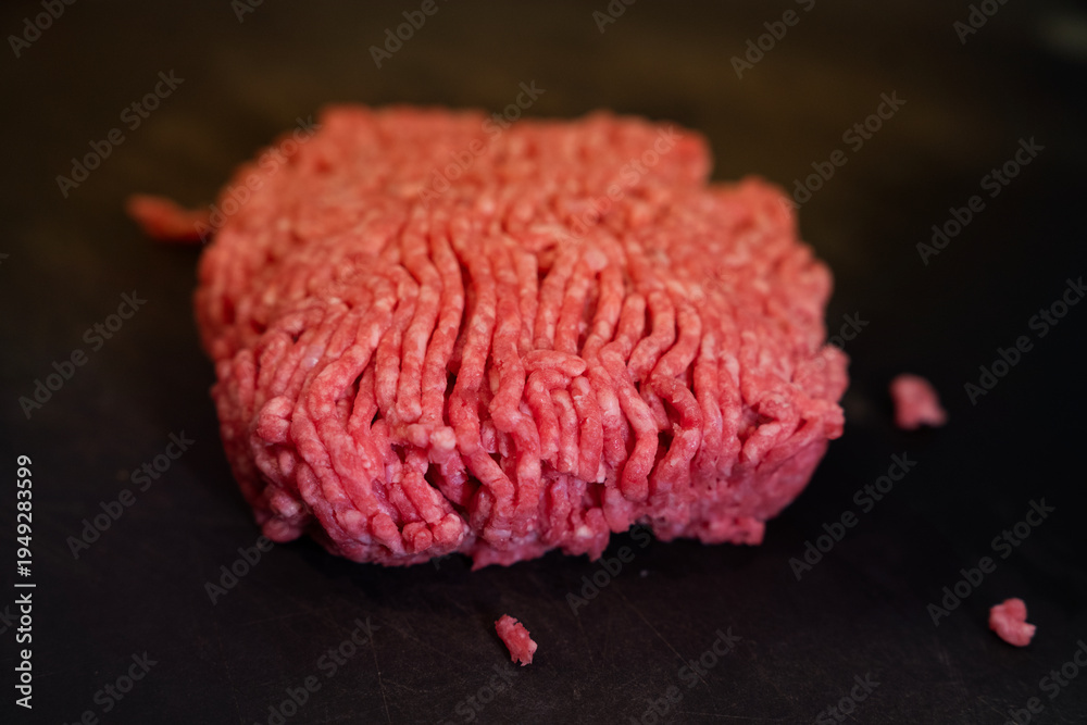 Obraz premium A detailed macro close-up shot of raw ground beef on a dark surface, highlighting the vibrant red color and texture. The shallow depth of field emphasizes the freshness and detail of the meat, perfect