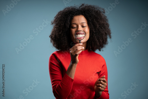 Close-up portrait of nice attractive funny foolish afro haired lady in red shirt  holding loupe showing teeth through isolated on blue pastel background