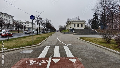 Photography Between the roadway of the street, along which cars pass, and the buildings, there is a sidewalk and a bicycle path with markings, paved with tiles