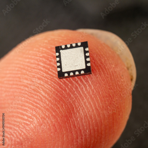 Obraz na plátně Bottom/pad side facing up, dark background
QFN microchip resting on a fingertip