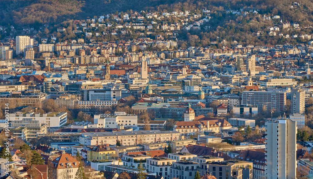 Fototapeta premium Panoramic view of Stuttgart city center in Germany during spring with warm golden evening light. Dense urban architecture, hills and residential districts captured from an elevated viewpoint.