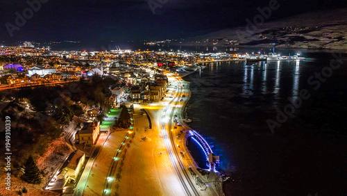 Drone view of Akureyri in North Iceland at night with illuminated bridge and city lights reflecting on water. Beautiful aerial scene of Akureyri harbor showing urban landscape and coastline in Iceland