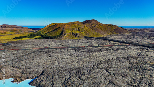 Drone view of the Blue Lagoon in Iceland with bright blue geothermal water surrounded by dark lava fields. Famous Iceland spa with steam, volcanic landscape, and tourists bathing in warm lagoon.