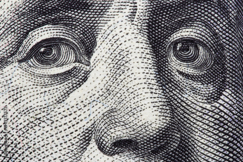  Extreme macro close-up of Benjamin Franklin's eyes on a one hundred US dollar bill. Business, finance and wealth concept. Concept of corruption, greed, bribery, or financial investigation.