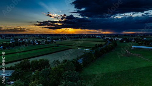 Photography A sunset fills the sky with orange and blue hues over a wide expanse of farmland