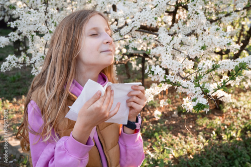 Young girl holding a tissue looking up near spring blossoms. Child hay fever, seasonal allergy concept.