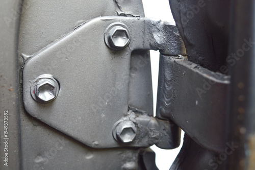 Close-up of a silver metallic car door hinge. Featuring heavy-duty hex bolts, industrial welding, and mechanical joint. Essential automotive hardware component.