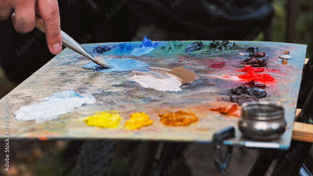 Fototapeta premium Painter mixing oil colors on palette with brush in art studio