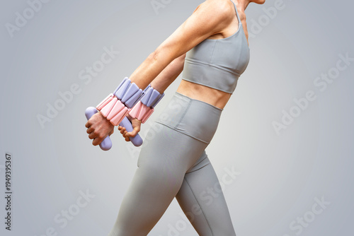 Sporty woman in gray activewear wearing adustable wrist weights and using hand weights