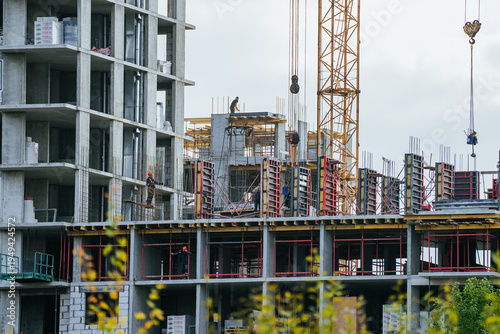 Construction workers efficiently building a large concrete residential building, using heavy equipment like a tower crane to construct modern urban housing infrastructure or a commercial property