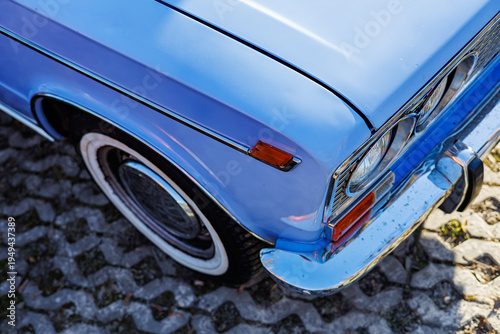 Φωτογραφία Close-up of a blue vintage car front: headlights, chrome grille and retro whitewall tires on a cobblestone road