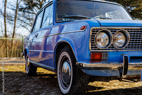 Obraz na plátně Close-up of a blue vintage car front: headlights, chrome grille and retro whitewall tires on a cobblestone road