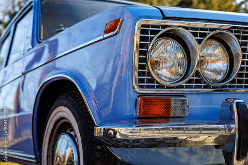 Canvas-taulu Close-up of a blue vintage car front: headlights, chrome grille and retro whitewall tires on a cobblestone road